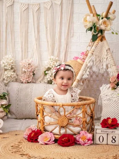 A smiling baby girl in her first birthday boho shoot. The wicker basket and 'One' sign are classic elements that mark this special milestone beautifully.
