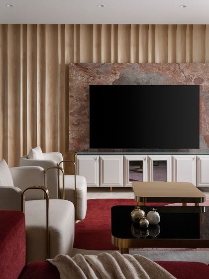 The living room at Haus of Aureus, where minimalism meets luxury. The space features a dramatic stone media wall, fluted wood paneling, and custom armchairs with elegant brass frames, all tied together with a bold red rug.