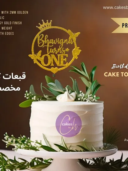 A mockup of the "Bhavigna turns ONE" glitter topper on a simple white cake, showing how it adds a pop of sparkle.