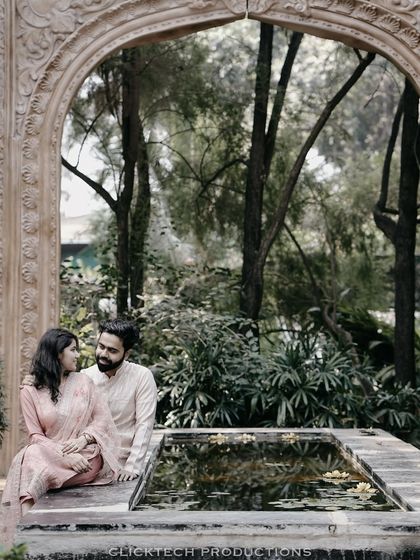 A serene moment by a lily pond, with a couple in traditional outfits sitting and talking, framed by a beautiful stone archway.