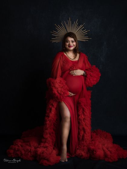 A portrait of a queen. This mom-to-be exudes power and confidence in a red gown and a golden sunburst halo against a black backdrop.
