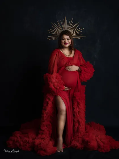 A portrait of a queen. This mom-to-be exudes power and confidence in a red gown and a golden sunburst halo against a black backdrop.