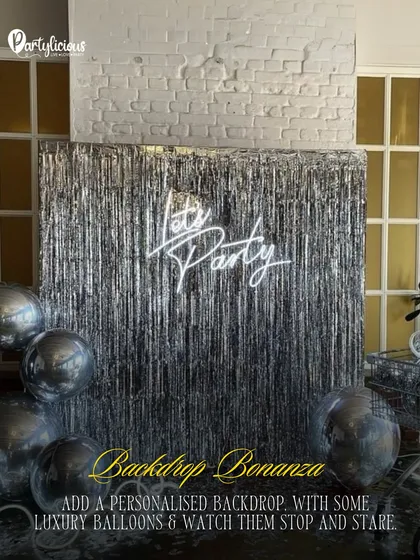 Backdrop Bonanza. A shimmering silver fringe backdrop with a 'Let's Party' neon sign and metallic balloons creates the ultimate party photo spot.