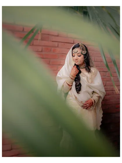Another artistic shot of Lubna, peeking through palm leaves, which adds a natural and intimate frame to her portrait.