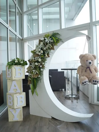 A dreamy 'Over the Moon' baby shower setup. A large crescent moon prop, adorned with flowers and a teddy bear, creates a magical photo opportunity.