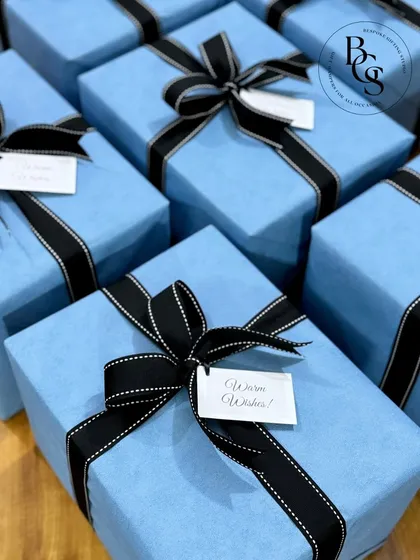 A collection of gifts wrapped in a beautiful powder blue, reminiscent of luxury brands. The simple black ribbon and "Warm Wishes" tag add a touch of sophistication, perfect for high-end corporate gifting.
