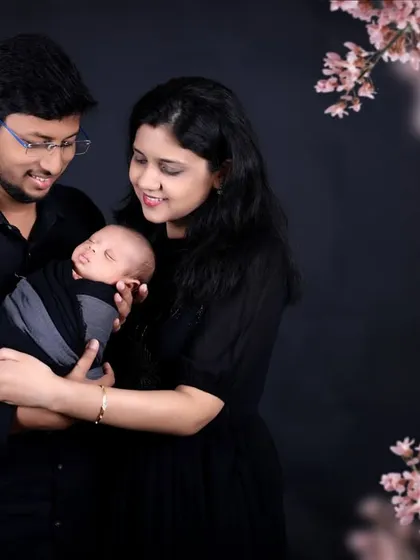 A serene family portrait framed by delicate pink blossoms. The parents lovingly hold their newborn, creating a beautiful and artistic image that feels both classic and modern.