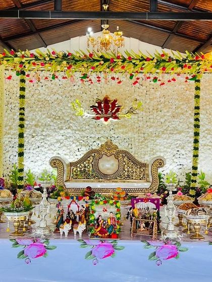 An elegant Seemantham stage with a backdrop made of white flowers. The setup is adorned with a central lotus cutout, traditional dolls, and a beautiful arrangement of offerings.