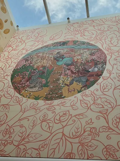 An upward-looking view of the installed "Mullai" panel, with its surrounding pattern of copper-colored leaves. The skylight above illuminates the earthy tones of the forest scene.