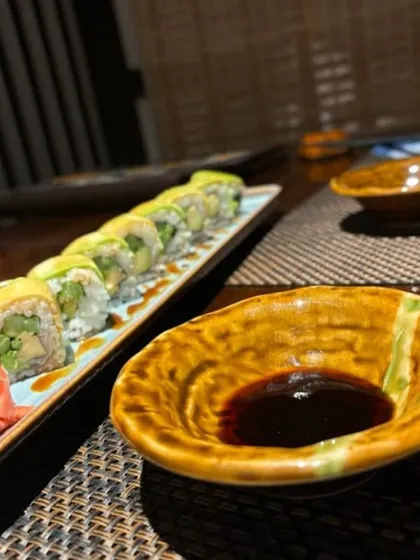 Our vegetarian Dragon Roll, featuring asparagus and cucumber wrapped in creamy avocado. It is served with soy sauce, pickled ginger, and wasabi for a complete and satisfying flavor experience.