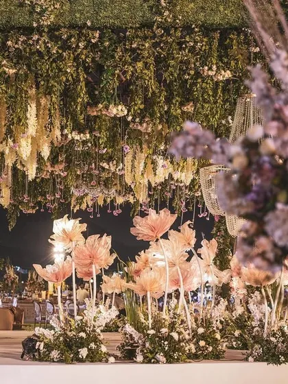 A beautiful, soft-focus shot of the reception decor, showing the layers of hanging florals and the whimsical paper flower installations. This image captures the romantic essence of the event.