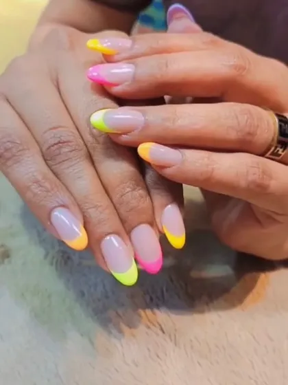 A playful and colorful French manicure. Each nail features a different neon tip in shades of yellow, orange, and pink for a fun, summery look.