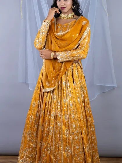 A full-length view of the mustard yellow chinon silk lehenga. The long-sleeved blouse and pleated skirt create a classic and elegant silhouette.