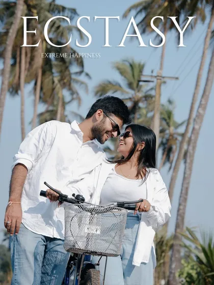 A bright and cheerful photo of a couple sharing a happy moment on a bicycle against a backdrop of Goan palm trees, representing a fun and casual pre-wedding photography style.