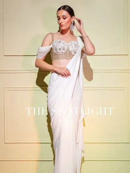 An angelic white drape saree with a structured, embroidered corset blouse. The off-shoulder drape adds a touch of ethereal grace.