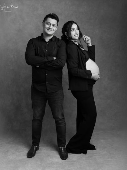 A stylish and playful black and white maternity shot. The couple stands back-to-back, showing off their fun-loving personalities in a classic studio setting.