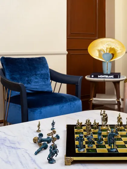 A quiet corner designed for contemplation. The rich blue velvet of the armchair, the elegant chess set, and the sculptural table lamp come together to create a sophisticated and inviting nook, showing how details build warmth and character.