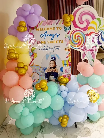 A welcome sign for Anay's "one sweet celebration." The sign is surrounded by a beautiful arrangement of pastel balloons and topped with large lollipop props.
