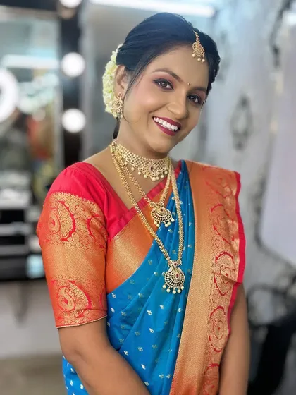 A smiling bride model showcasing a classic South Indian bridal look with a blue and red Kanjeevaram saree.