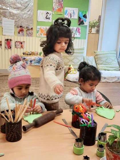 This scene shows different stages of playdough exploration happening at once. One child rolls, another uses cutters, and a third observes, demonstrating how open-ended materials cater to individual interests and developmental levels.