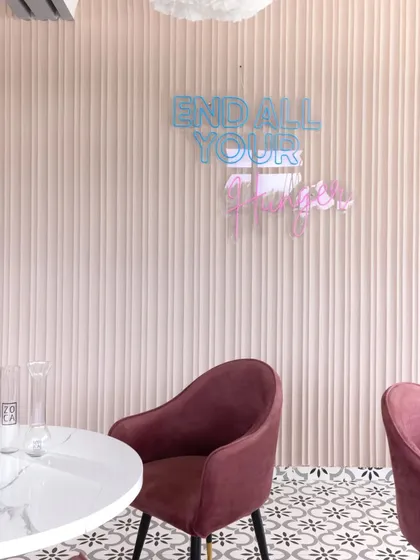 A playful neon sign adds a touch of modern fun to the pastel-colored, fluted wall at the Zoca rooftop café.