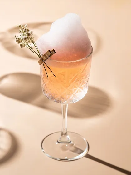 A delicate, light-filled cocktail with a cotton candy cloud. This photo showcases a bright and airy style, perfect for a whimsical or daytime drink menu.