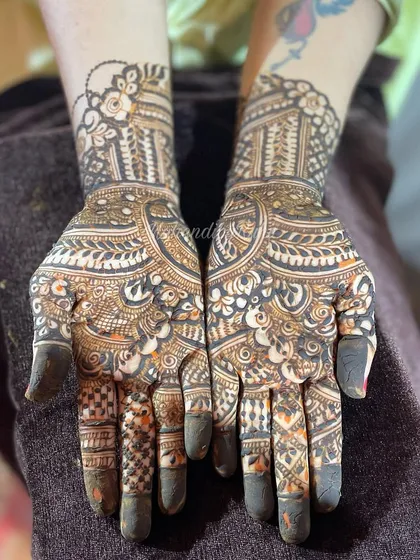 This design incorporates negative space with leafy cutouts on the forearm. The palms are filled with a dense mix of traditional patterns, and the fingers have detailed cap work.