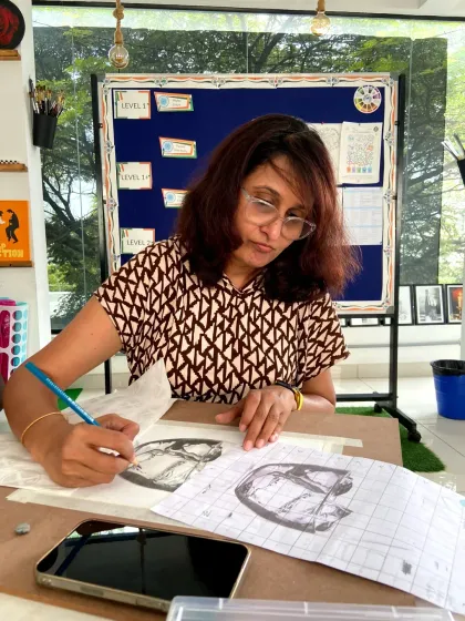 This student is learning to sketch, using a reference photo to guide her drawing of a glass object.