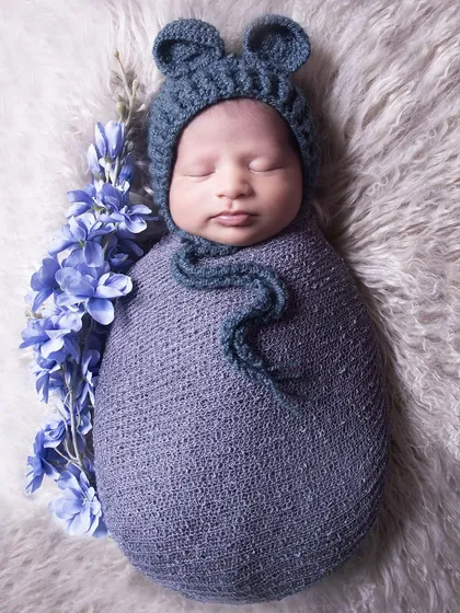 A simple and sweet portrait of a newborn in a blue bear-eared hat, swaddled and sleeping on a soft white fur blanket.