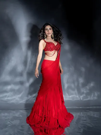 A full-length shot showcasing the stunning silhouette of the red gown against a moody, textured studio background.