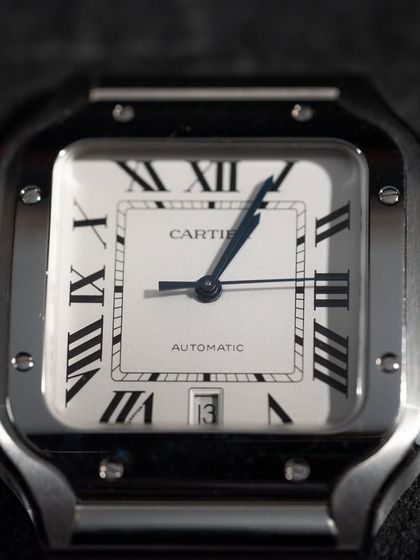 A close-up of the classic Cartier Santos dial. The elegant Roman numerals, blued-steel hands, and guilloché center square are all hallmarks of this iconic design.