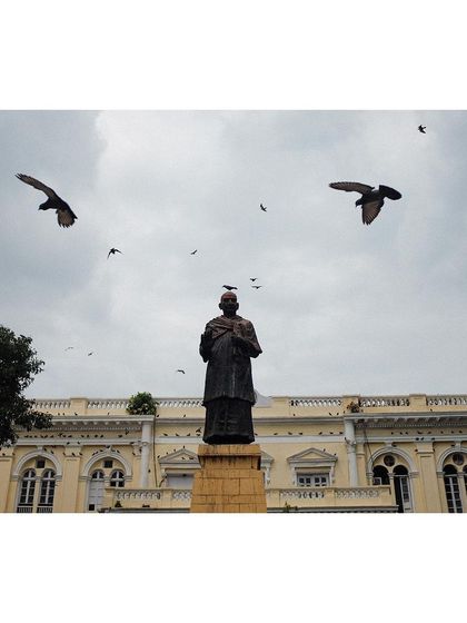 The statue of Indian independence activist Swami Shraddhanand in Delhi, with pigeons flying overhead. The shot captures a moment of history against a cloudy sky.