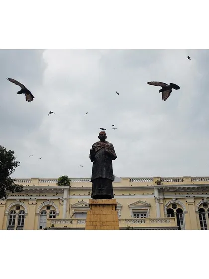 The statue of Indian independence activist Swami Shraddhanand in Delhi, with pigeons flying overhead. The shot captures a moment of history against a cloudy sky.