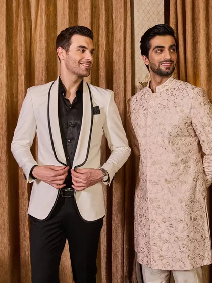 This image perfectly captures my range, showing a classic embroidered sherwani next to a sharp white tuxedo with black detailing. I can create the perfect look, whether your style is ethnic or Western.