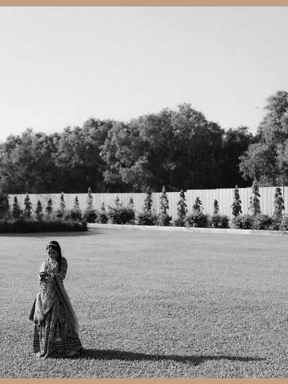 A wide, minimalist black and white shot of the bride standing alone in a large field. The composition emphasizes her solitary grace and the quiet moments of reflection before the ceremony.