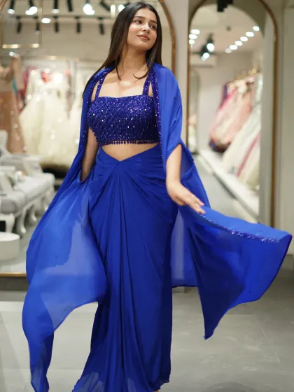 I love mixing tradition with a bit of drama, and this Indo-Western set is the perfect example. It features a modern draped skirt with a stunning embellished crop top and a flowy cape, all in a striking royal blue. It’s comfortable, chic, and made to stand out.