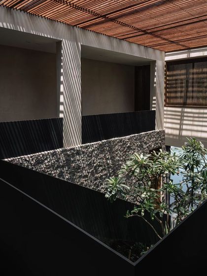 An overhead view of the central courtyard, showcasing the multi-level design and the use of raw stone and wood. A frangipani tree grows in the center, acting as a living sculpture.