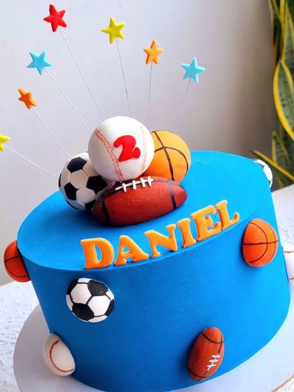 A sports-themed cake featuring a variety of hand-sculpted fondant balls, including a baseball, basketball, soccer ball, and football.