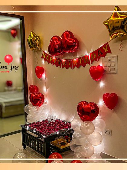I can turn any room into a romantic retreat for a birthday surprise. This bedroom decoration includes a "Happy Birthday" banner, heart and star-shaped foil balloons, fairy lights, and a table centerpiece with delicate rose petals.
