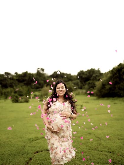 A magical shot of the mom-to-be in a floral dress, surrounded by falling pink petals. It’s a whimsical and beautiful portrait.