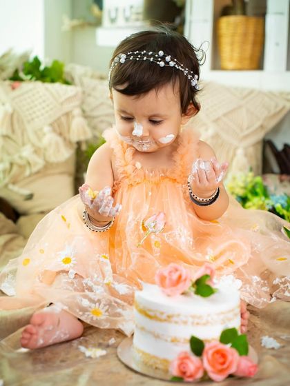 This little one is completely focused on her cake, a sweet and funny moment from her first birthday session. The delicate details on her dress and the simple cake are a beautiful combination.