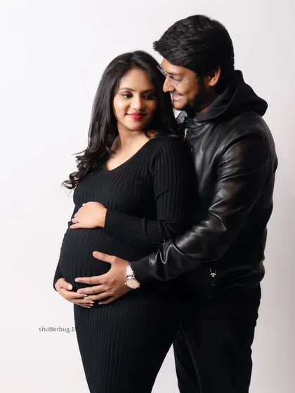 A sweet and simple couple's portrait against a clean white background. Their casual black outfits and the gentle way they hold the baby bump make for a warm and modern maternity photo.