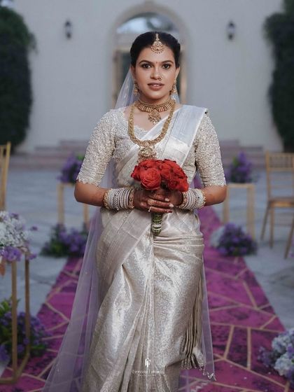 The bride in her silver saree, holding a bouquet of red roses, ready for her ceremony.