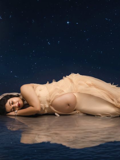A dreamy and artistic concept, showing the mom-to-be sleeping under a starry night sky with a beautiful reflection.