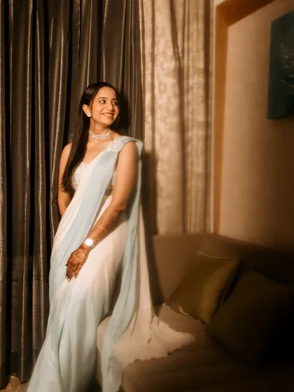 An elegant standing portrait of the bride. The warm, soft lighting and classic pose highlight the beautiful drape of her saree and her graceful demeanor.