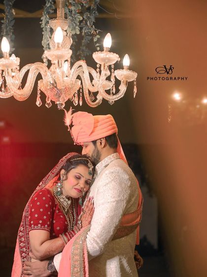 A romantic wedding portrait with the bride resting her head on the groom's chest, both framed by a beautiful chandelier.