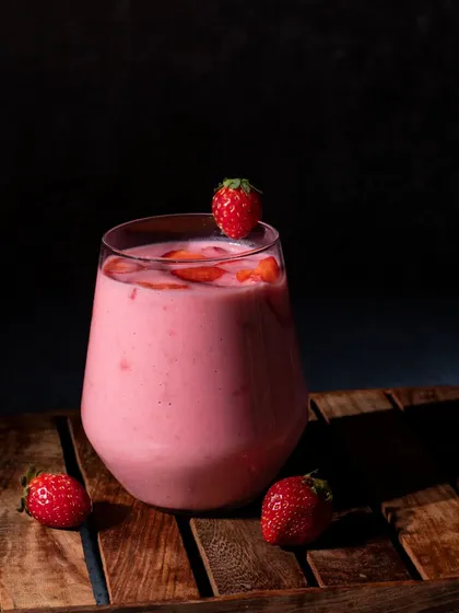 A dark and moody shot of a strawberry milkshake. The lighting highlights the texture of the drink and gives it a rich, indulgent feel.
