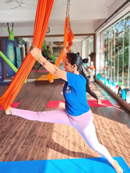 Using the aerial silk for support, a student works on a standing split variation. The silk provides stability, allowing for a deeper and more controlled stretch.