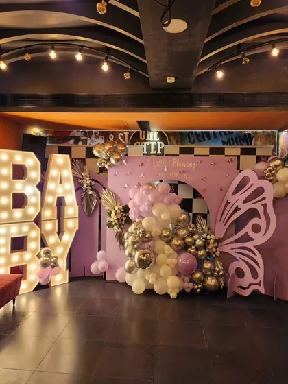 A stylish baby shower setup with large "BABY" marquee letters and a butterfly-themed backdrop. The purple, white, and chrome gold balloons create a chic and modern look.