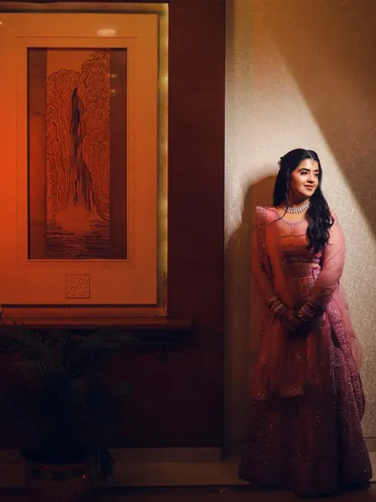 A full-length portrait of the bride in her pink engagement lehenga. The single light source creates a beautiful play of light and shadow, making her stand out.